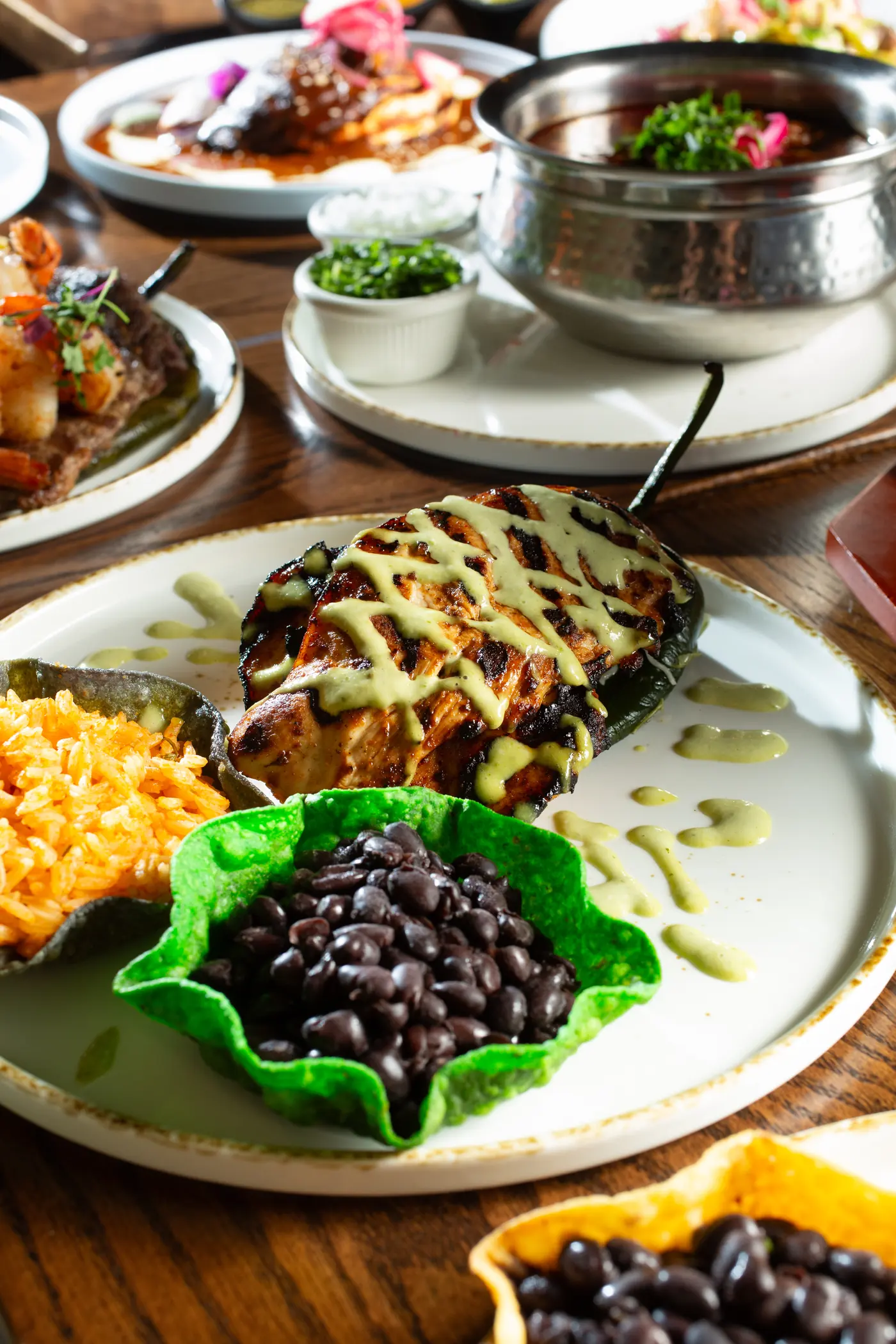 Grilled chicken drizzled with a pale green crema over a roasted poblano, with Mexican rice and black beans in tortilla cups
